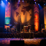 Palco de festival musical com iluminação colorida e instrumentos preparados para uma apresentação internacional