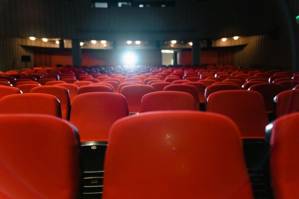 Sala de cinema vazia, com fileiras de poltronas vermelhas voltadas para uma tela iluminada