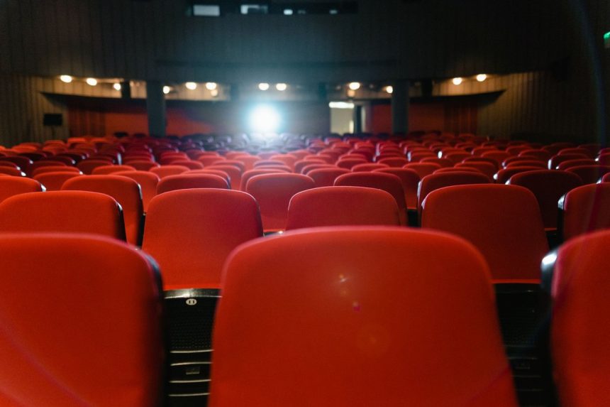 Sala de cinema vazia, com fileiras de poltronas vermelhas voltadas para uma tela iluminada