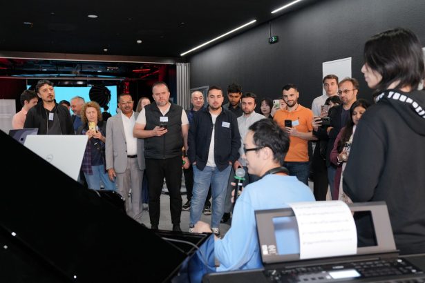 Público diverso acompanha atentamente uma demonstração de piano em um ambiente interno.